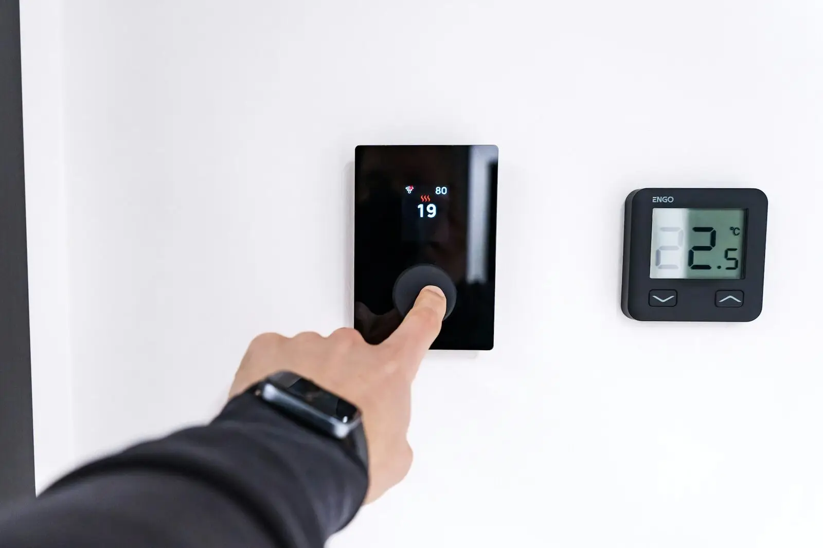 Hand die een thermostaat aan de muur bedient